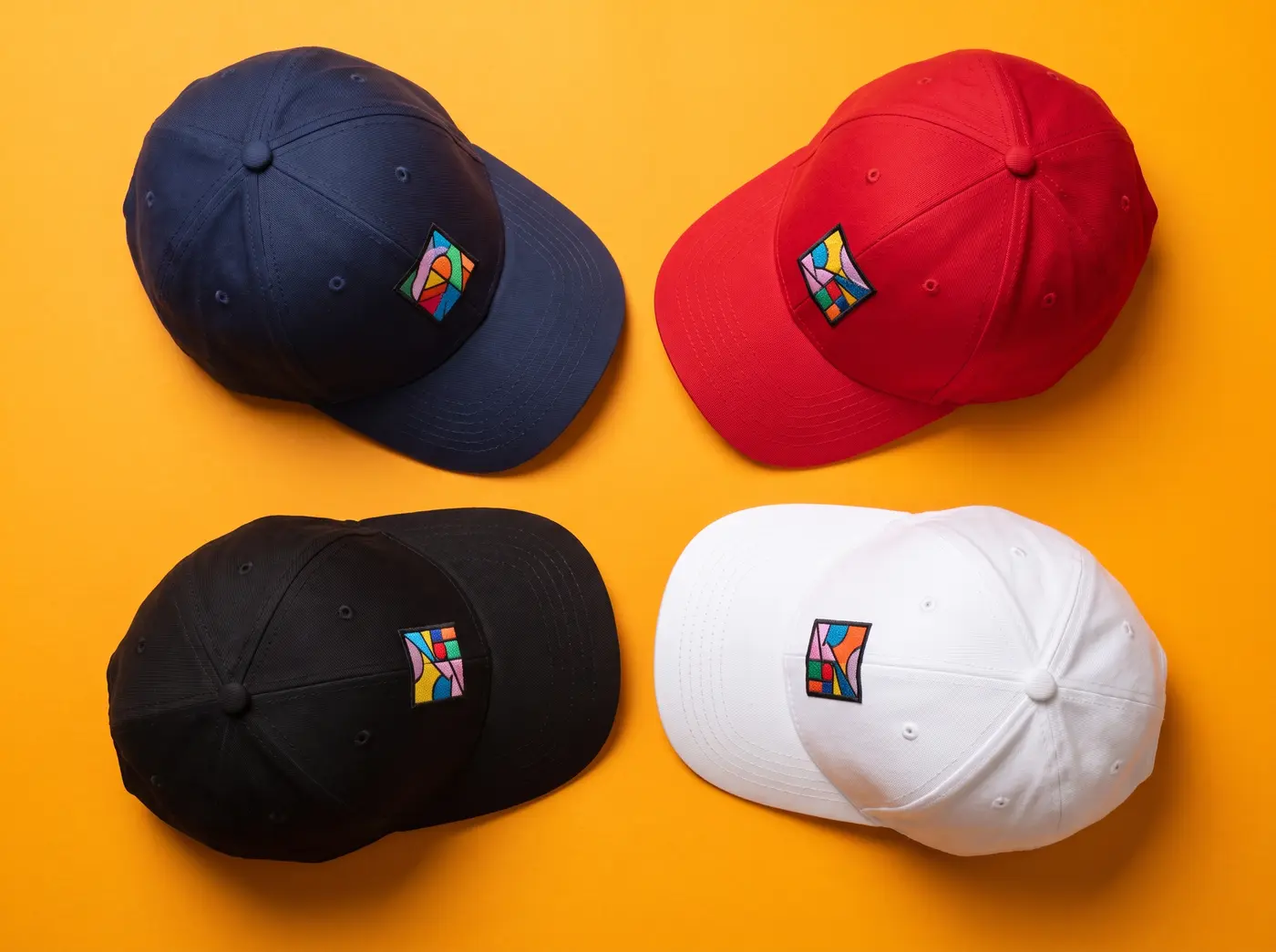 Vier bedruckte Caps in Navy, Rot, Schwarz und Weiss auf orangem Hintergrund